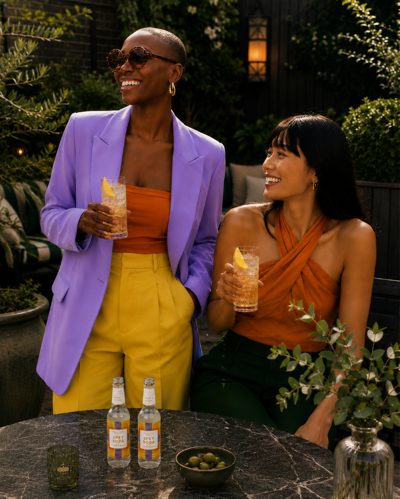 Two women laughing at an outdoor patio table, each holding a Whisky & Spey Soda. 